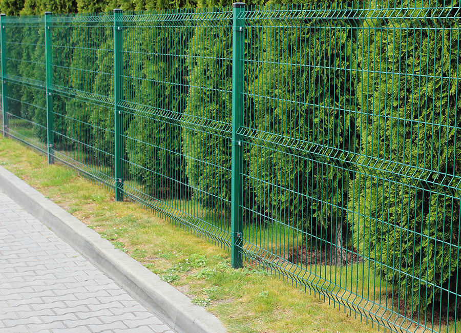 Clôture en treillis soudés vert, en acier, longeant une haie d'arbustes