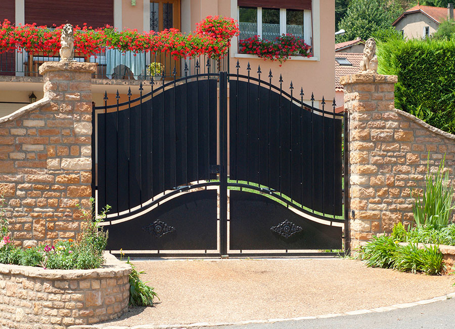 Portail battant en fer forgé, magnifiquement encadré par un muret maçonné avec des pierres de taille